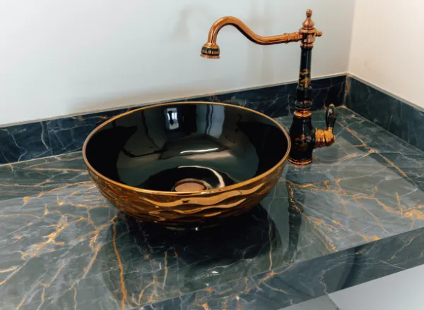 Lavabo com cuba de apoio e torneira em acabamento dourado sobre bancada de mármore