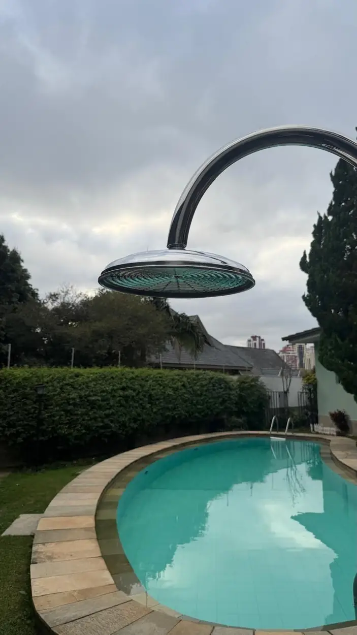 Ducha externa em inox polido com braço curvo instalada em área de piscina residencial
