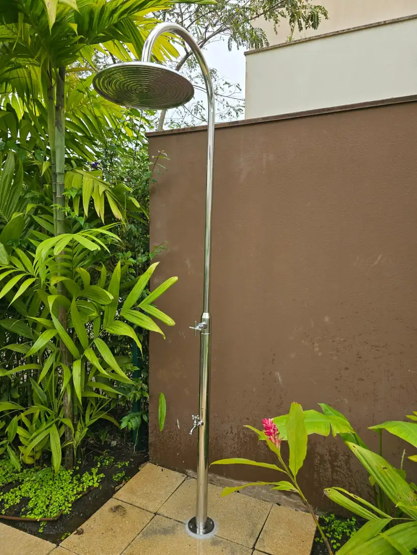 Ducha externa em inox polido com registro e lava-pés instalada em área externa arborizada