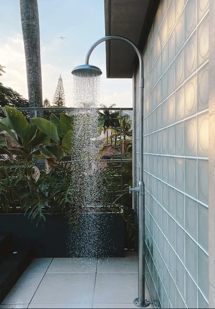 Ducha externa em inox instalada em terraço com parede de blocos de vidro