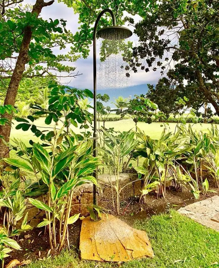 Ducha externa sob medida em acabamento escuro instalada em jardim com vista para o gramado